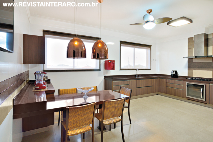 A cozinha é pura elegância com piso em porcelanato Travertino (Portobello Shop), armários planejados amadeirados (Florense), bancadas em granito Marrom Café (Marmoraria Exclusive) e luminárias cobre (Luminá Iluminação). Pintura da Tintas e Texturas Maggicor e metais da Duo