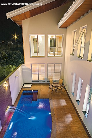 Amplos panos de vidro se abrem para a área da piscina revestida com pastilhas de porcelana azul. O painel e o piso em porcelanato Ecowood, da Portobello Shop, garantem um ar aconchegante ao espaço externo. As mesas e cadeiras são da MAC Móveis