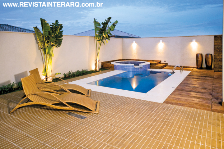No espaço de lazer, espreguiçadeiras em fibra repousam sobre o piso elaborado com mix de cerâmicas. Com revestimento em pastilha, a piscina tem borda em cimentício e deck com revestimento que imita pranchas em madeira de demolição.