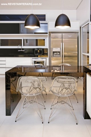 Branco e preto foram as cores escolhidas para a cozinha, que tem armários planejados e piso em porcelanato. Prática, a bancada em granito preto acompanha cadeiras em acrílico Charles Eames (Robusti). Os pendentes pretos têm detalhes internos em alumínio escovado