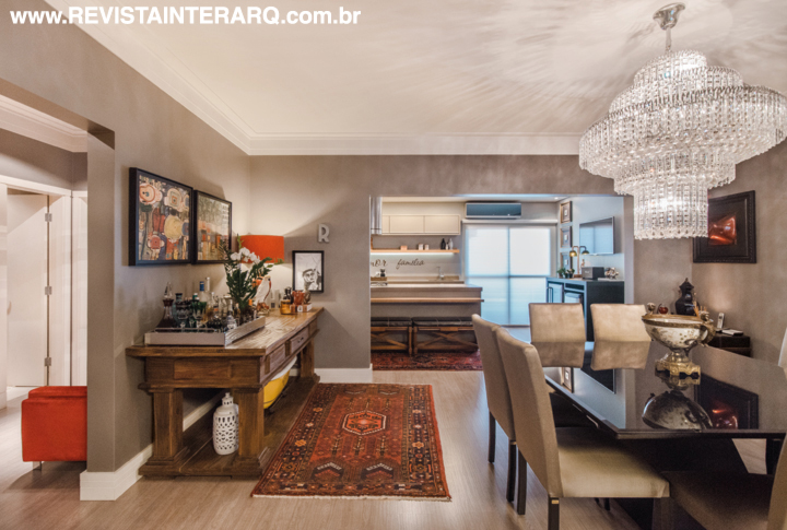 Em todo o apartamento, a designer utilizou piso em madeira clara (Ateliê Revestimentos Roberto Cervellini) e paredes nos tons Cinza Elefante e Prata envelhecido da Suvinil (Depósito das Tintas). Na sala de almoço integrada à cozinha gourmet, o aparador em madeira de demolição (Vitória Régia) acomoda o bar. A luminotécnica é bem pontuada, com lustres de cristais, pendentes, plafons e abajures (Ponto de Luz).