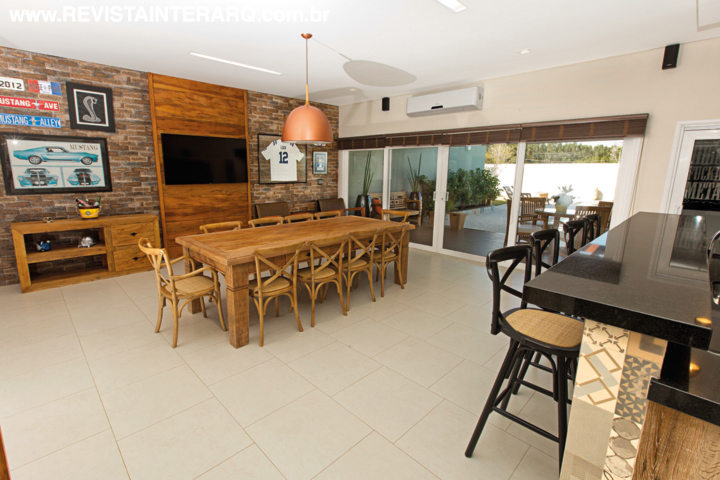 O espaço gourmet é o local preferido da casa e conta com um excelente equipamento de som ambiente. Os móveis de demolição, como a mesa e aparador são da Center Móveis, assim como as cadeiras em madeira e ratan. As portas de correr se abrem para a varanda, posicionada sob a pérgola de madeira e vidro (Vidraçaria Colorado), e para a área da piscina