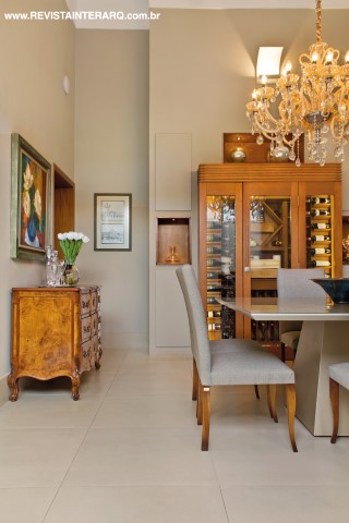 A adega climatizada com acabamento em madeira é a protagonista da sala de jantar, que conta ainda com mesa em laca e vidro (Decorativa), cadeiras (Sierra Perfil Casa) e cômoda bombê (Decorativa)