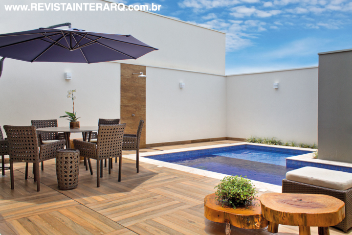 Na área da piscina, o porcelanato amadeirado funciona como deck e acomoda a mesa com ombrelone. O projeto arquitetônico é de Marcus Ávila