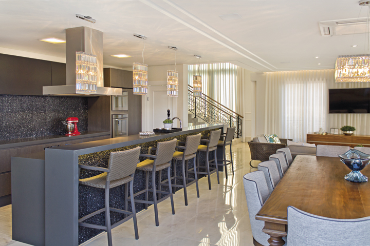 A cozinha faz parte do social e, por isso, ganhou bancada em Caesarstone cinza e pastilhas de mármore Nero Marquina sob quarteto de luminárias de cristal