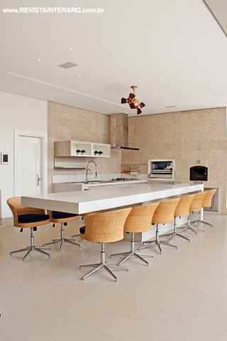 A área da churrasqueira conta com forno à lenha, chopeira, cooktop, balcão refrigerado (Refrigeração Araçatuba) e uma grande bancada em CaesarStone (Rolsilva Marmoraria). A parede foi revestida com minipastilhas de mármore e pedra ônix. Cadeiras, mesa e banquetas da Sierra Perfil Casa