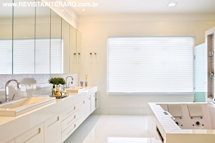 Todo branco com bancada em Marmoglass (Rolsilva Marmoraria), o banho do casal conta armários espelhados e laqueados (ambos da Roso Móveis). Persiana Lumiere da Paraíso Carpetes. Toda a residência foi automatizada (Home Systems) para facilitar o dia a dia da família