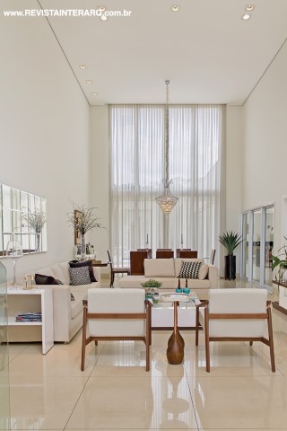 A luz natural invade a ala social da casa graças ao generoso painel envidraçado revestido com delicadas cortinas de gaze de linho (Paraíso dos Carpetes). A leveza visual é completada pelo lustre de cristal, poltronas e mesinhas laterais (Destack Móveis)