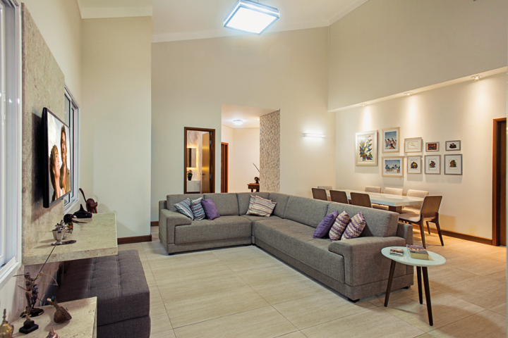 living ambientado com sofá em “L”, almofadas da Magnificat e painel em mármore Travertino Anticato. Piso em porcelanato da Villa Bella Acabamentos. O projeto arquitetônico é de Thales Porlan de Oliveira