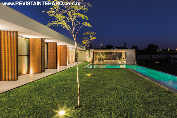 Os quartos e a área gourmet vislumbram a piscina com raia, revestida com pedras da Indonésia (Ponto Bello). O fechamento dos ambientes é feito com portas de alumínio preto e vidro (Esquadrias 2 Irmãos) e painéis de ripas de madeira trançadas