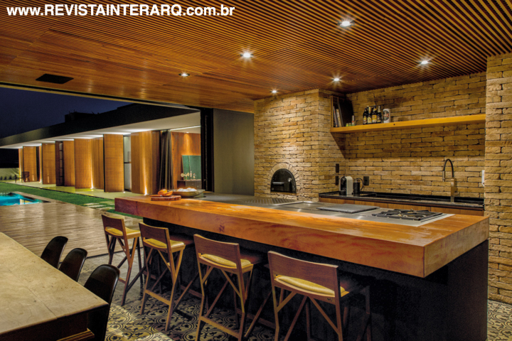 Na área gourmet, forno de pizza e bancadas em granito preto (Marmoraria Granart), madeira e inox. Na parede, pedras da Pedras Mundial