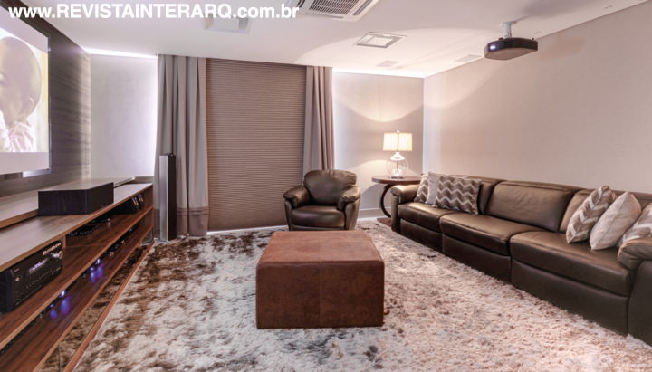 O home theater ganhou persianas blackout da HunterDouglas (ACB Casa), sofá em couro marrom com mecanismo automatizado e a poltrona giratória (UneRobusti). Sobre a mesa lateral, abajur em vidro da Casa Verão. O móvel em madeira da Florense acomoda os equipamentos e apoia a tela em vidro e projetor da AutoMundi. Tapete da Bidjar e iluminação dimerizada da Luminá Iluminação