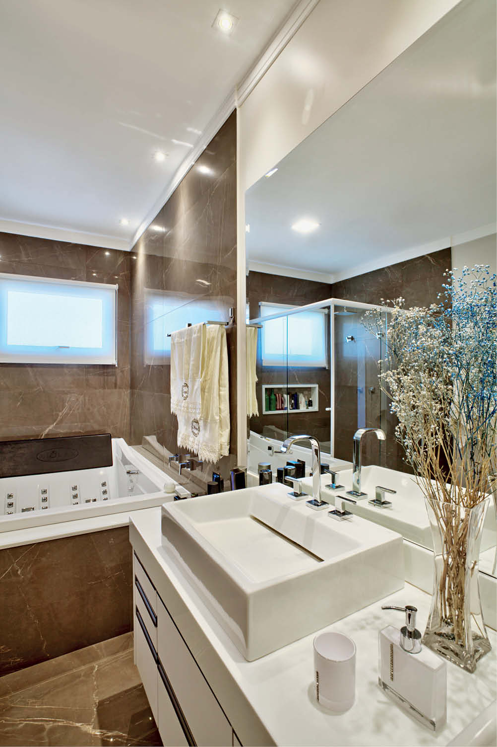 O banho do casal em porcelanato e bancada em Nanoglass branco conta com Spa duplo.