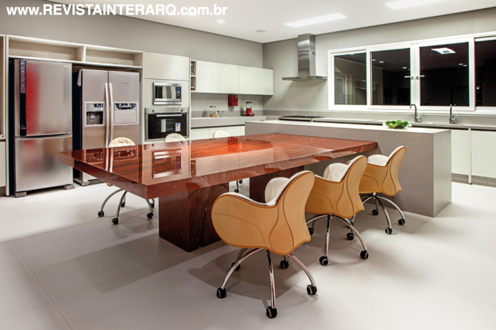 Da cozinha, onde a grande bancada em mármore vermelho (Multipedras Mármores e Granitos) funciona como mesa para refeições rápidas. Os armários planejados da Ornare combinam com a bancada em lâmina porcelânica. Eletros e coifa da Elettromec. Toda iluminação é da Dessine