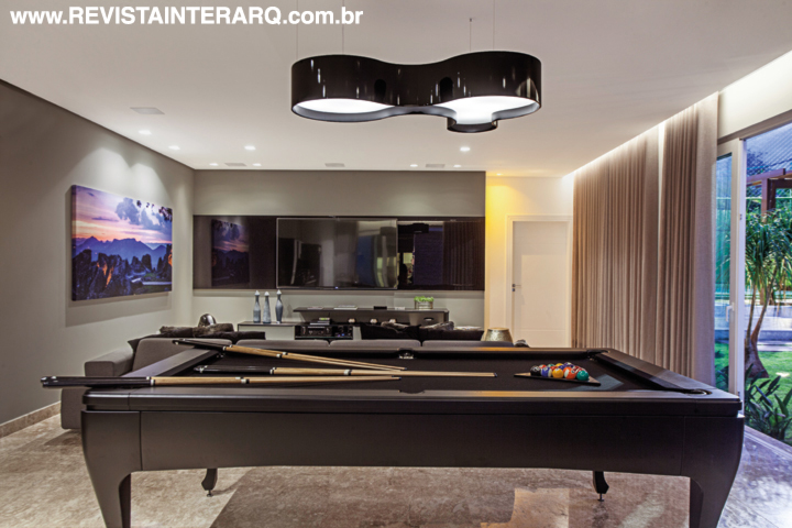A sala de jogos com mesa de bilhar preta e luminária de formas orgânicas. Portas de correr com vidros da Vitral