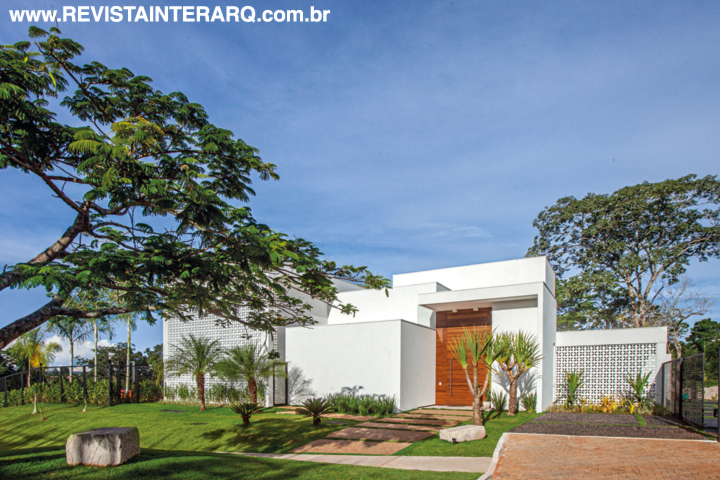 O layout todo branco contrasta com o jardim (paisagismo de Fabio Camargo) e a madeira da porta de entrada
