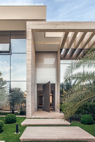 A pérgola em mármore Travertino (Marmoraria Alvorada) emoldura a entrada principal da casa com porta da Cinex (Abito)