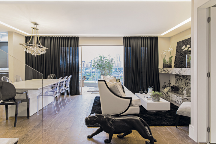 Mármores exóticos, como o Esplendor Gold da lareira, estão entre os destaques do duplex. No social, uma grande mesa de banquetes, ladeada por cadeiras Louis Ghost pretas e transparentes, está sempre à espera dos amigos. Cortinas, tapete e a “pantera” negra evocam luxo 