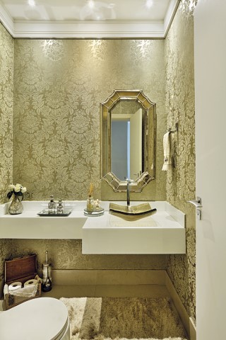 A iluminação com embutidos e lustre de cristal destaca detalhes do lavabo, como o papel de parede dourado arabescado, a bancada em Nanoglass e os metais e cuba de vidro. O projeto arquitetônico original é de Alberto Paganelli Barbour
