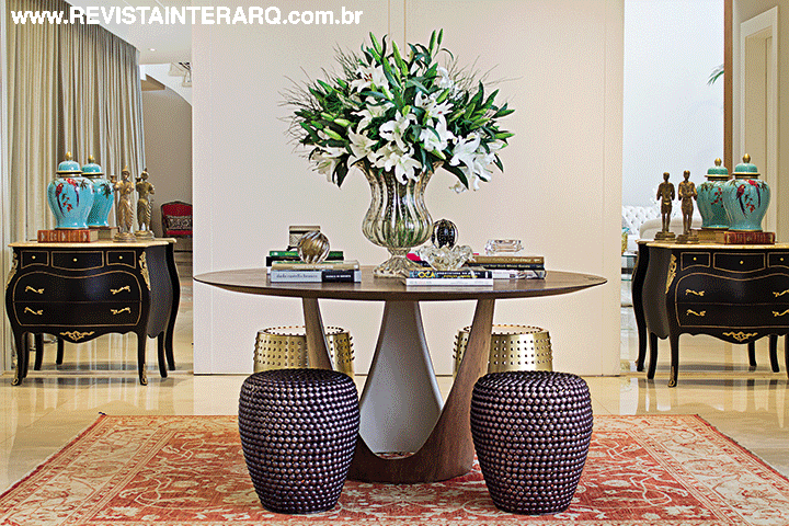 No hall de entrada, a moderna mesa circular e os garden seats em latão e metal preto (Decorativa) fazem contraponto ao tapete e às cômodas Bombé escuras em frente aos espelhos (Vidraçaria Rio Preto). Os Muranos são da Krieê Decorações