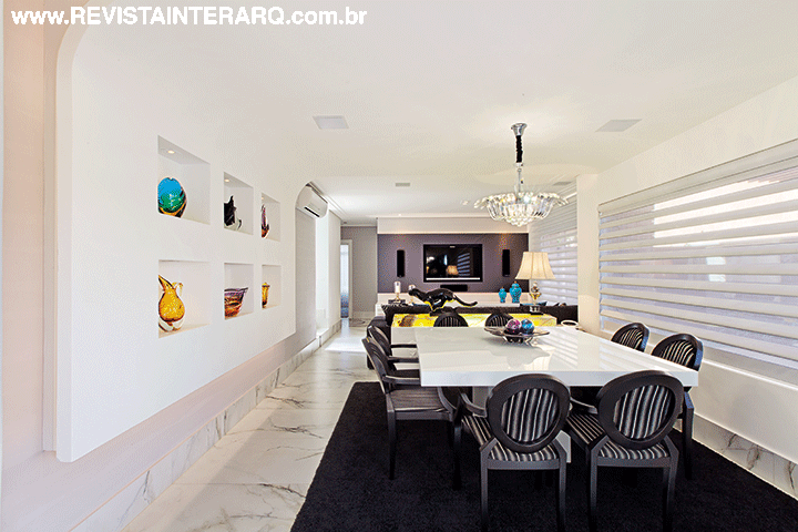 A eterna combinação do preto com o branco foi a escolha para todo o design de interiores da casa. Jantar e TV revelam esse contraponto de luxo, com piso em porcelanato Paonazzetto (Portobello Shop), tapete preto Avanti (Decorativa) e mesa em vidro branco (Sierra Perfil Casa) acompanhada por releituras da cadeira medalhão. Persianas Pirouette, da Hunter Douglas (Griffe A), agregam suavidade à composição. Destaque para o buffet branco com tampo de ônix. Toda a casa foi automatizada com equipamentos de última geração. Com apenas um toque, o morador escolhe as cenas de luz, temperatura e o playlist a ser ouvido em todos os ambientes O painel com acabamento curvo em gesso acomoda os Muranos (Krieê Decorações e Jackie Móveis)