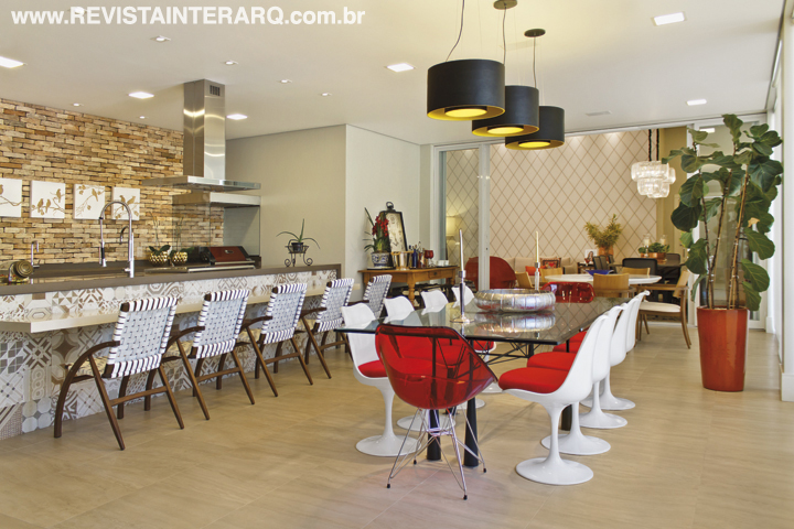 O espaço gourmet foi pensado para receber convidados em dias festivos, com uma grande mesa de vidro com cadeiras vermelhas (Perfil Casa) sob o trio de pendentes (NR Iluminação) e cadeiras Flexa (Jackie Móveis) junto à bancada da churrasqueira. 