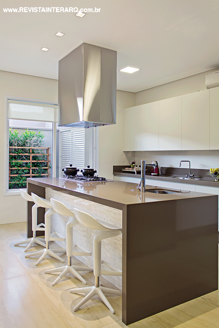 Na cozinha, a bancada em Caesarstone se destaca entre as banquetas e armários brancos (Movelaria Polidoro). O piso é em porcelanato da Portobello Shop e a iluminação é da NR Iluminação
