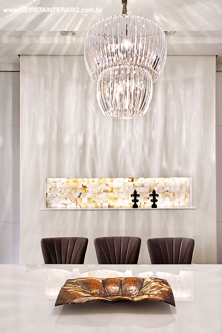 O painel em pedra ônix translúcida e iluminada é o protagonista da sala de jantar. As esculturas em forma de Flor de Liz estão entre as preferidas da arquiteta pelo simbolismo de poder, honra e lealdade