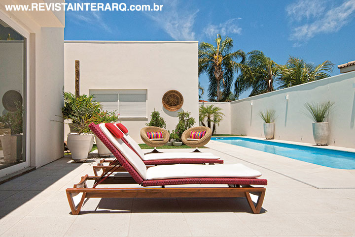 No lazer, o piso em cimentício da Castelatto (Ponto Bello Acabamentos) no entorno da piscina contrasta com os jardins e móveis de design contemporâneo das espreguiçadeiras de madeira e poltronas de fibra da Saccaro (Galeria Top Kazza | Saccaro)