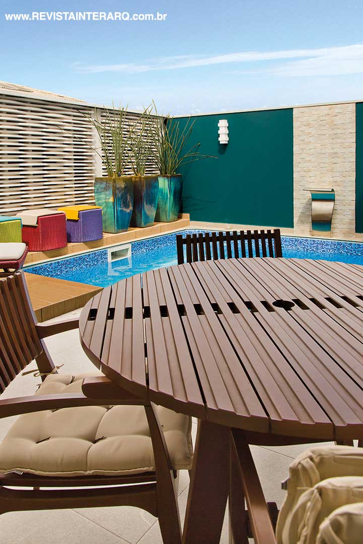 Na piscina, o revestimento cimentício filetado (Ponto Bello Acabamentos) faz contraponto ao verde-petróleo da parede lateral. Os móveis em madeira e fibras coloridas (Galeria Top Kazza | Saccaro) dão um charme especial ao ambiente. A arquitetura da casa é assinada por Michele Damasceno e o paisagismo é de Mônica Costa