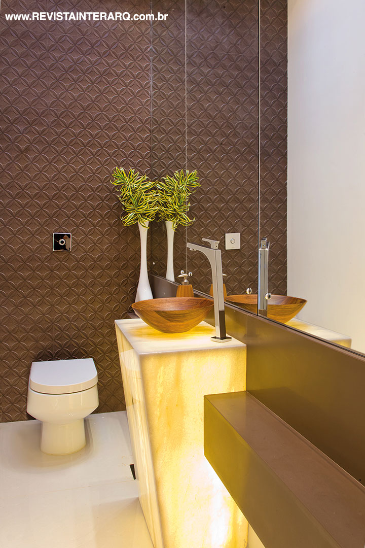 No lavabo, a protagonista é a pedra translúcida retroiluminada, emoldurada pela bancada em Silestone (Fran Mármore). Metais e louças da Hidromar