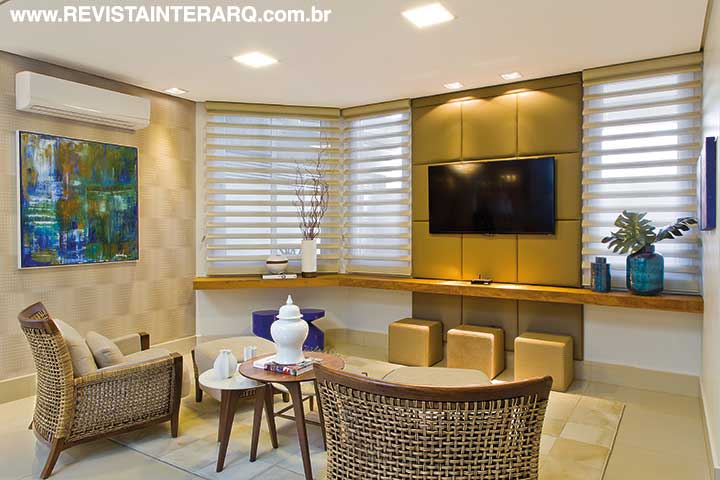 Na sala de TV, o elemento principal é o painel em couro, emoldurado por charmosas cortinas horizontais (Marcello Revestimentos) e pela prateleira de madeira de demolição. O aconchego do espaço foi garantido pelo tapete de couro e pela textura da trama das poltronas com design exclusivo (tudo da Galeria Top Kazza | Saccaro). A tela e os bancos azuis dão um toque de cor ao ambiente. Objetos decorativos da Casa de Cora