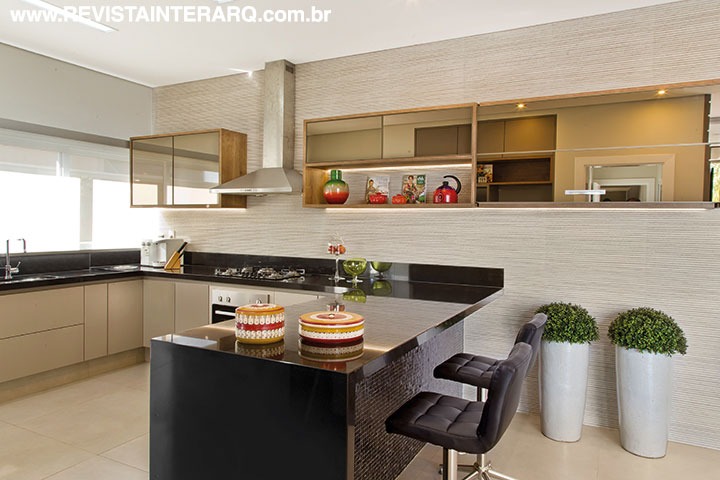 O charme da cozinha é a parede do fundo que recebeu revestimento em ranhuras e armários com acabamento em espelho bronze. A bancada é em granito Preto Absoluto