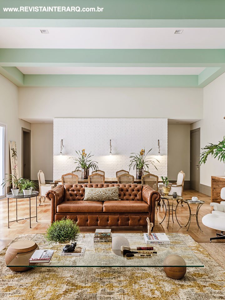 O social surpreende com a modernidade dos detalhes verdes no teto e o design da mesa de centro em contraponto ao sofá Chesterfield em couro e cadeiras de jantar de estilo (tudo da Firmato Móveis)