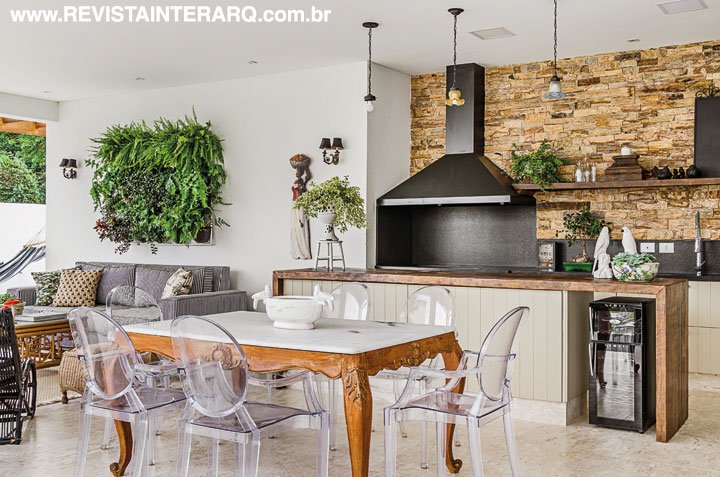 Na área gourmet, mais contrastes em harmonia, com parede de pedras (Astral Mármores), planejados claros e cadeiras Ghost em acrílico (Firmato Móveis) acompanhando a mesa antiga
