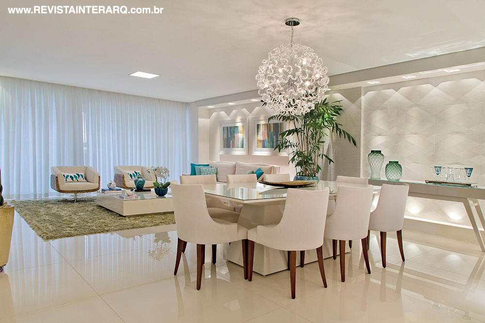 A unidade visual do social é acentuada pela simetria dos nichos com iluminação embutida no gesso e pelo piso único em porcelanato de grandes medidas. O jantar soma a beleza de linhas retas da mesa e aparador em laca com as formas orgânicas do lustre de cristais (Reflexo Iluminação). Os acessórios são da Stylo & Classe