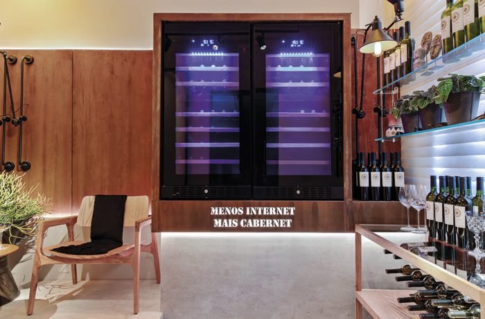Com um convite aos amantes de vinho “Menos internet, mais cabernet”, o ambiente Nossa Adega, assinado pelo arquiteto Antônio Bettarello, possui paredes em aço corten da Alupoli e móveis em madeira natural que se destacam na adega.
