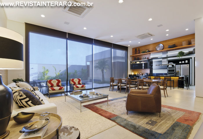 A área social desta casa projetada por Ariana Bastos é toda integrada à área de lazer. Para dar unidade visual, foi utilizado o piso em porcelanato da Casa dos Construtores. O espaço possui linguagem clean com living, sala de jantar (Perfil Casa) e gourmet. As persianas controlam a entrada de luz natural que atravessa as portas de vidro e alumínio da LA Esquadrias. A pintura suave é da São Geraldo Tintas